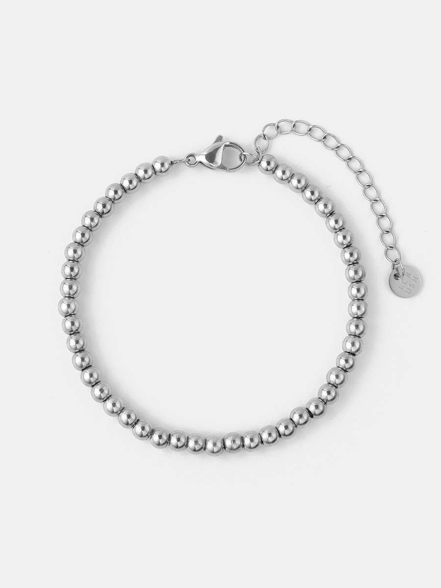 Silberfarbenes Kugelketten-Armband mit Karabiner, Verlängerungskette und Anhänger vor hellem, einfarbigem Hintergrund.