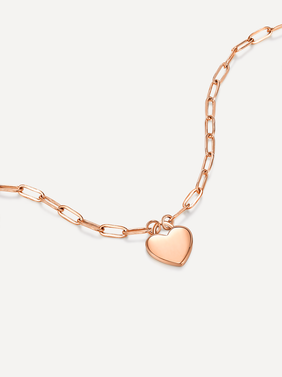 Roséfarbene Gliederkette mit Herz-Anhänger als Armband auf weißem Untergrund.