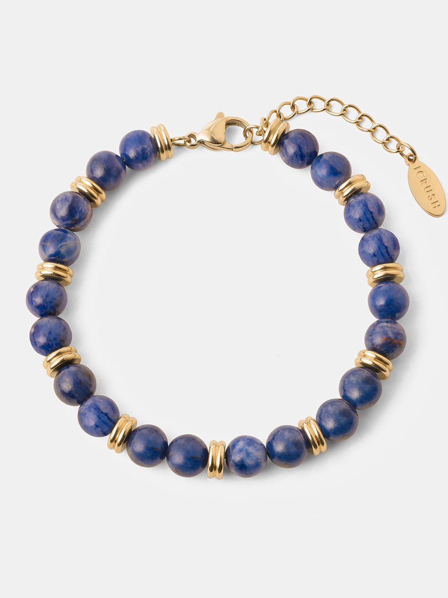 Armband mit goldfarbenem Verschluss, dunkelblauen Lapislazuli-Kugeln und Zwischenringen, liegend.