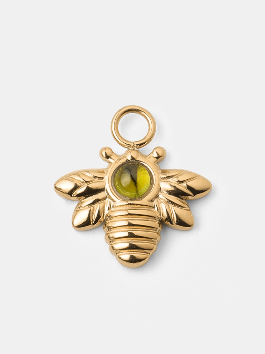 Goldener Bienen-Charm mit grünem Steinchen, Öse, Flügeln und Rippenmuster, frontal auf neutralem Untergrund.