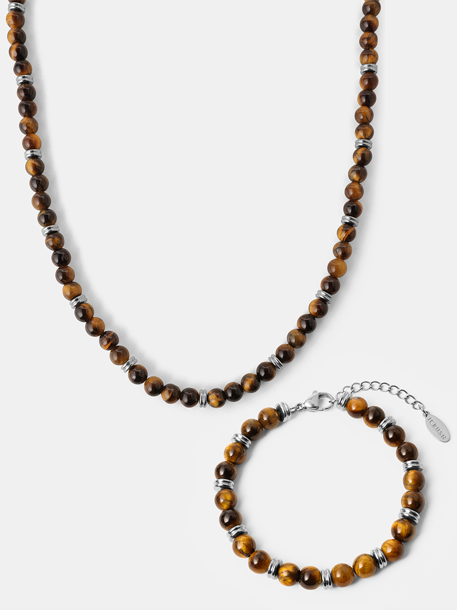 Halskette und Armband mit runden Steinperlen aus Tigerauge, silberfarbenen Zwischenstücken und Verschluss auf grauem Hintergrund.