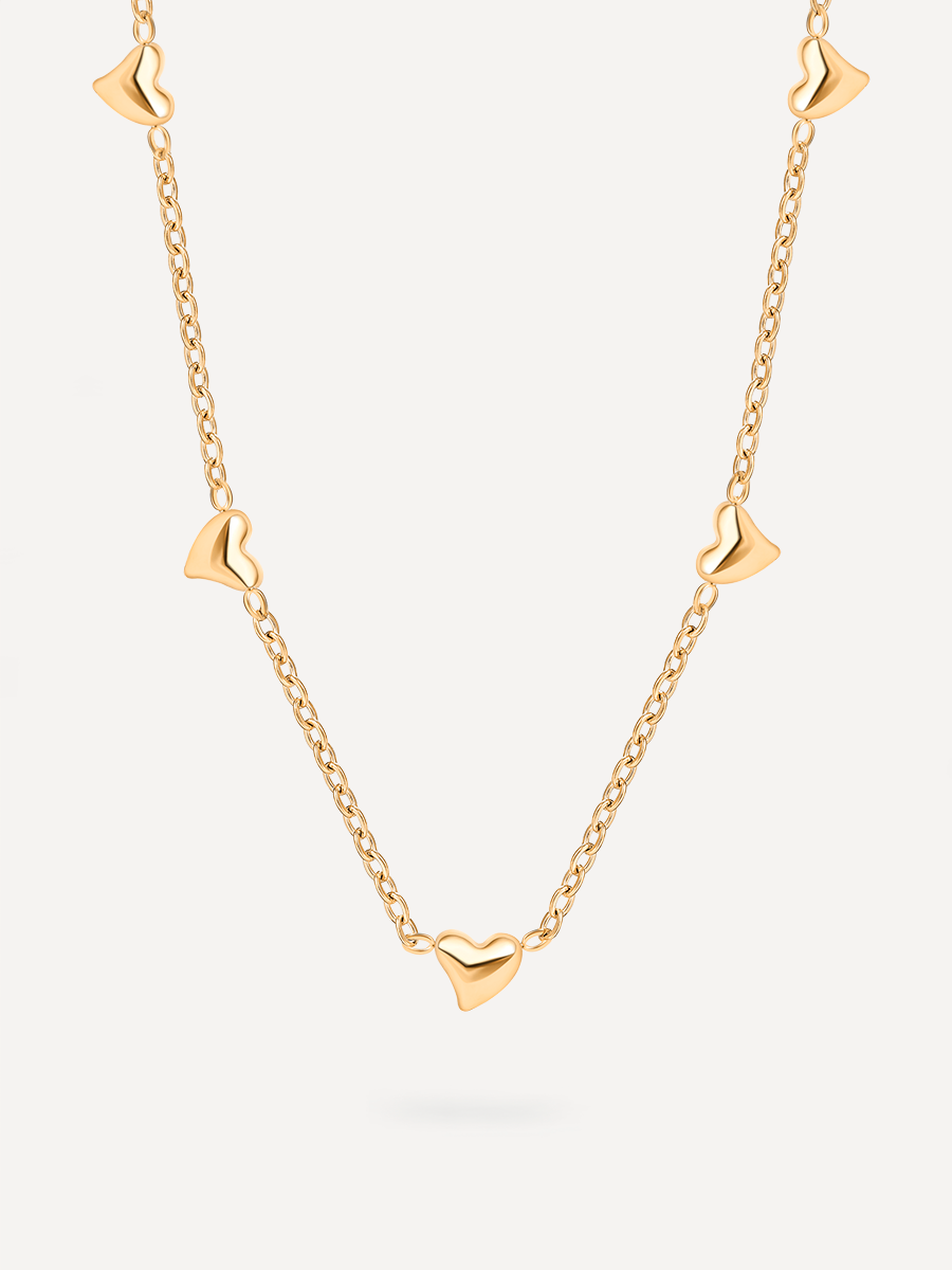 Flach liegende Goldkette mit verteilten Herzelementen und glänzender Kettenstruktur auf neutraler Fläche.