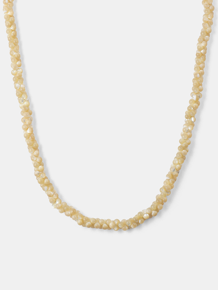Goldfarbene Perlenkette aus facettierten Muschelperlen, U-Form, vor neutral hellem Hintergrund.