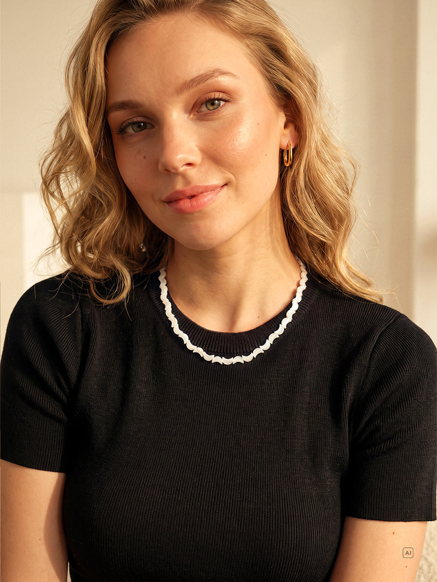 Goldfarbene Lunar Strand Kette mit gewellten, milchig hellen Gliedern am Hals einer Blondine im schwarzen Shirt.