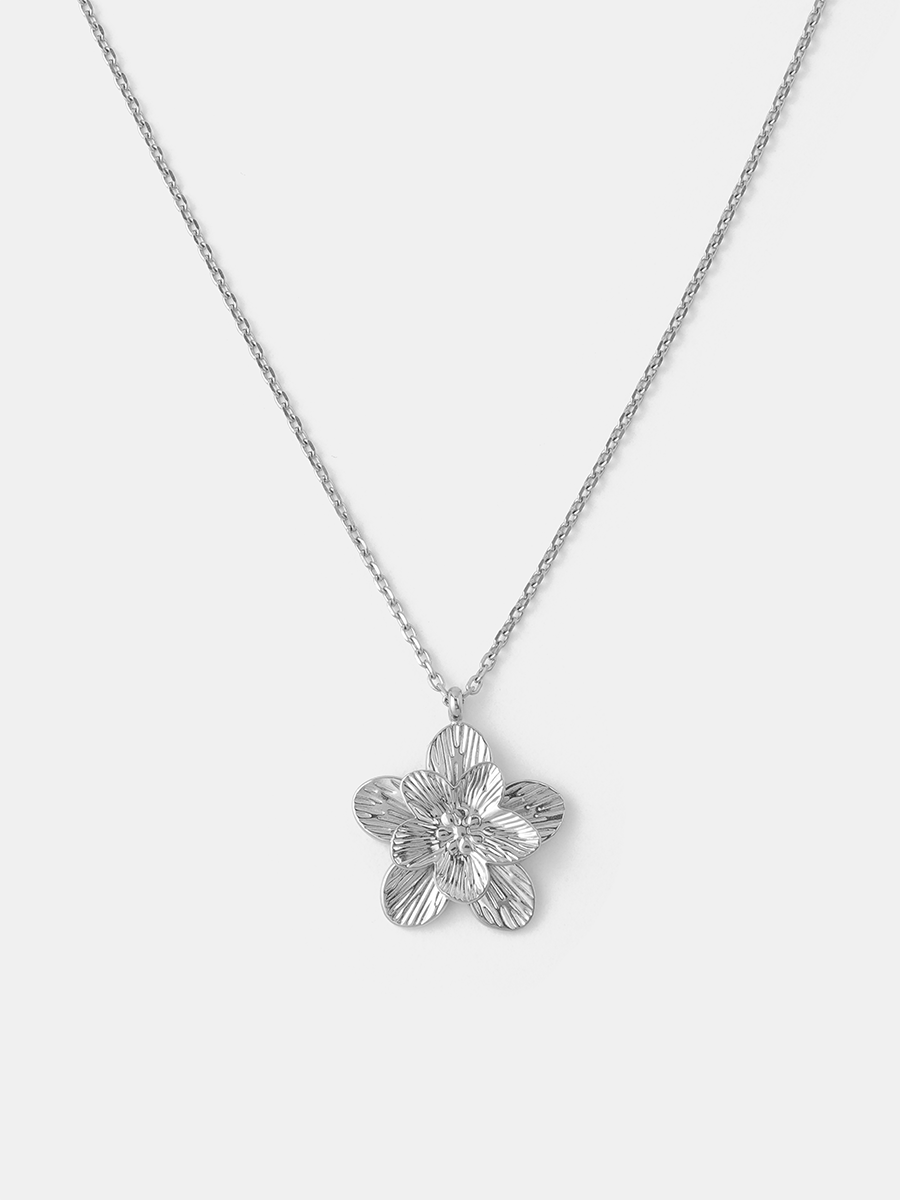 Kette in Silberoptik mit floralem Anhänger, fein geriffelte Blütenblätter, schlichter heller Hintergrund.