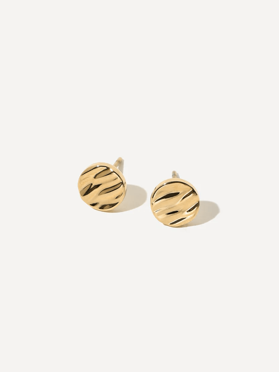 Goldfarbene Ohrstecker mit wellenartigem Relief, einer präsentiert Stecknadel, vor neutraler Fläche.
