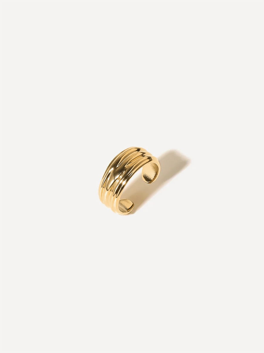 Goldfarbene Ohrklemme mit Rillen, offener Ring, liegt auf heller Fläche, Schatten rechts.