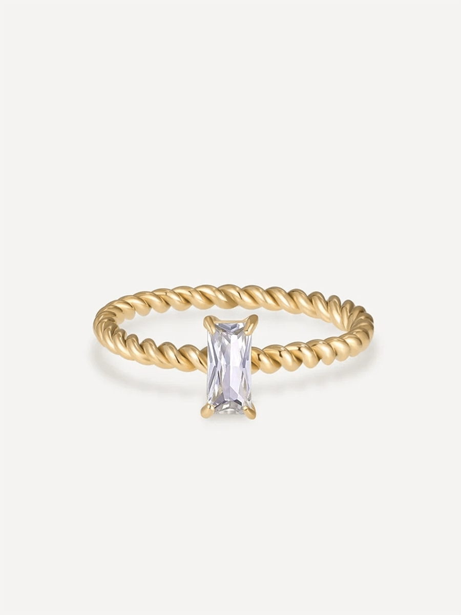 Goldener Ring mit schraubenförmigem Seilband und funkelndem, rechteckigem Stein, frontal vor schlichtem Grau.