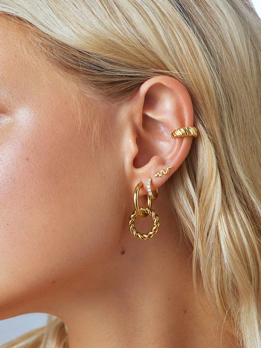 Nahaufnahme eines Ohres mit blonden Strähnen und mehreren goldenen Ohrringen, darunter eine funkelnde Creole.