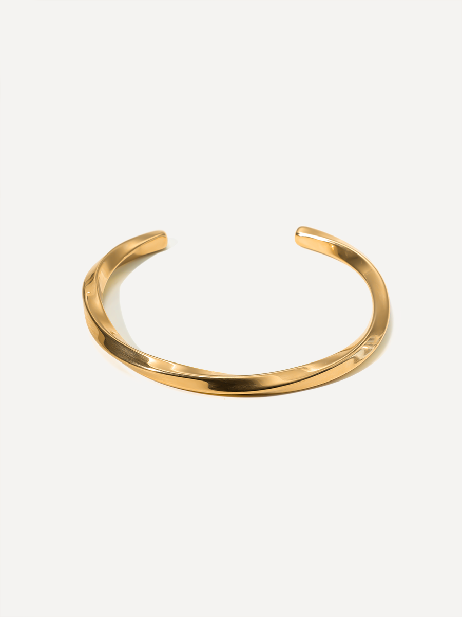 Glänzender goldfarbener Armreif, offen und rund, einzeln vor neutralem, hellem Hintergrund.