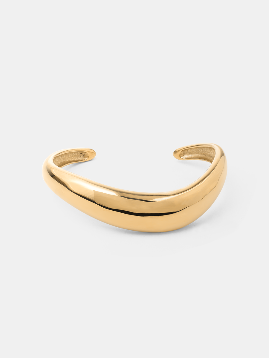 Glänzender goldfarbener Armcuff mit offenen Enden auf schlichtem weißem Untergrund.