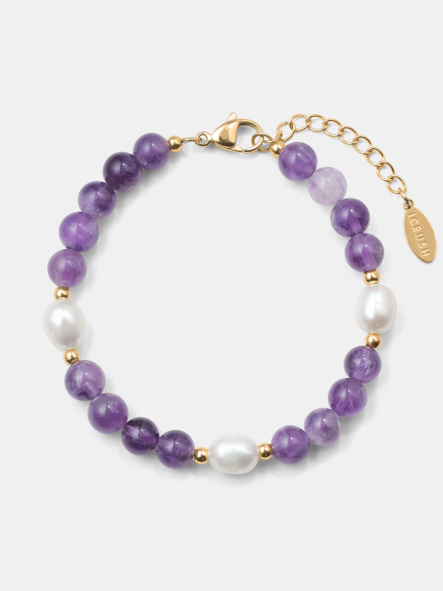Goldfarbenes Armband mit violetten Amethyst-Rundperlen, weißen Perlen und Verlängerungskette auf hellem Hintergrund.