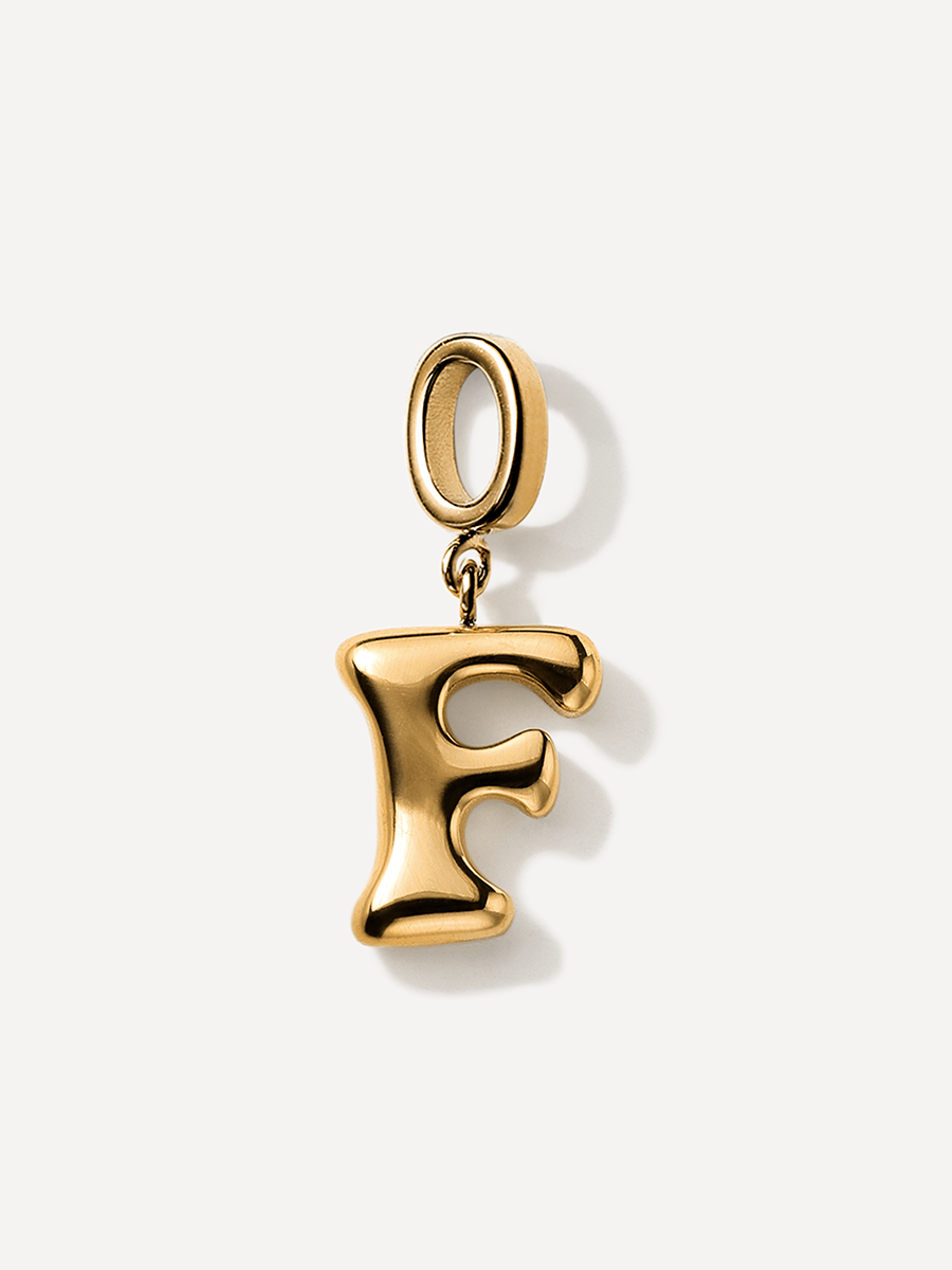Goldener Buchstabe F als bauchiger Charm, runde Aufhängeöse, kleiner Verbindungsring, glänzend, heller Hintergrund.