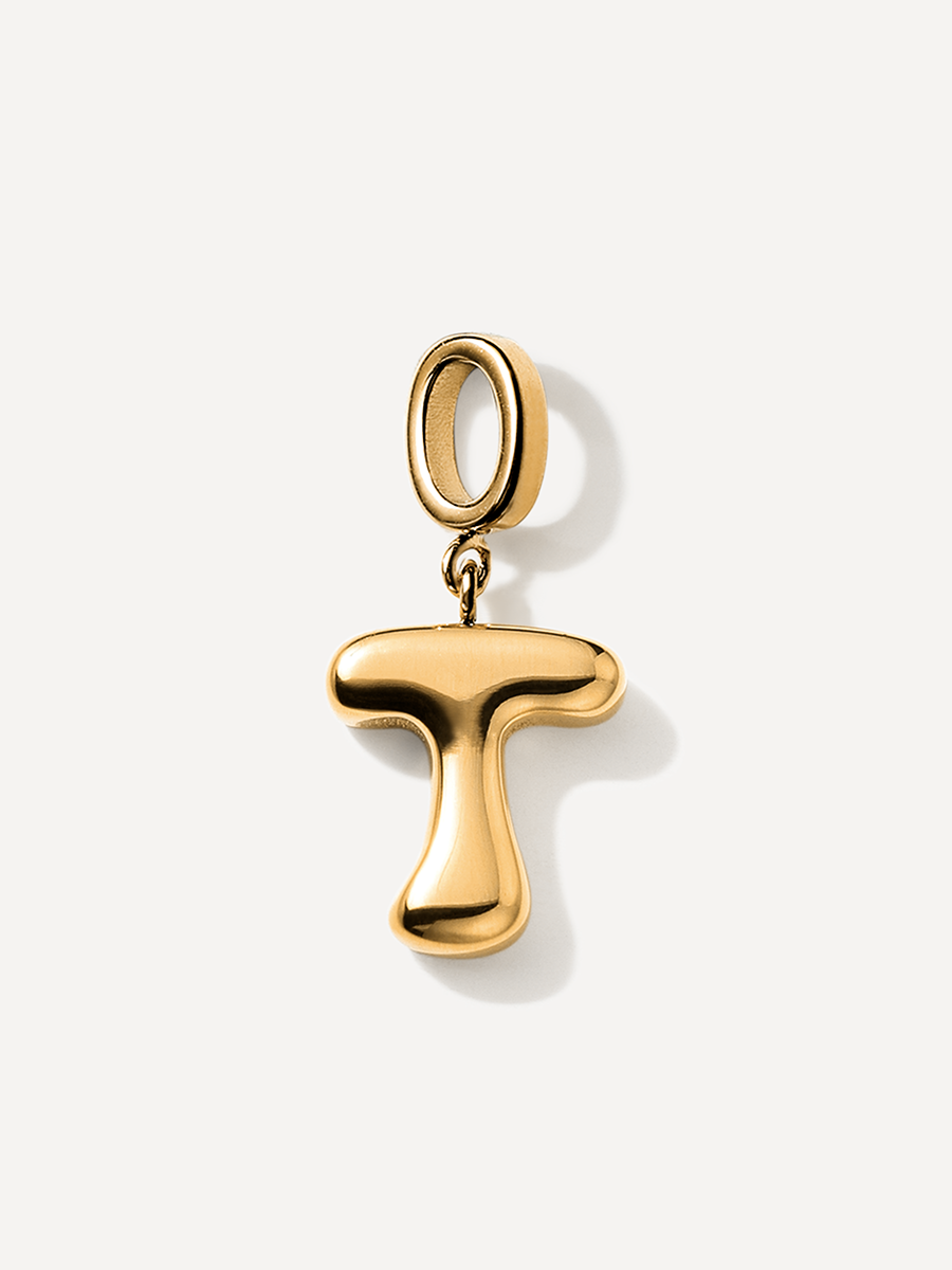 Goldener T-Buchstaben-Charm, wulstig und glänzend, ovaler Aufhänger mit kleinem Ring, vor hellem Studiohintergrund.
