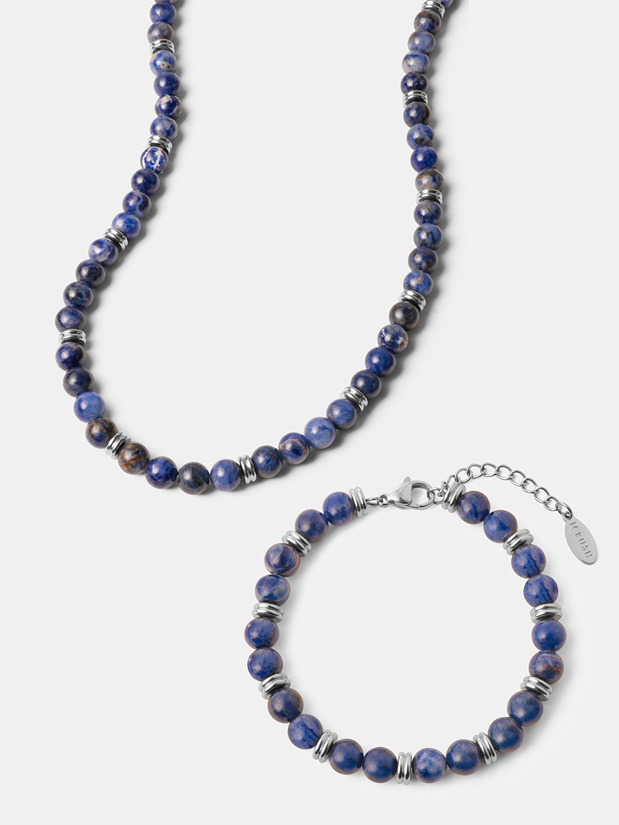 Armband und Kette aus dunkelblauen Kugeln mit silbrigen Zwischenringen und Verlängerungskette auf hellem Untergrund.