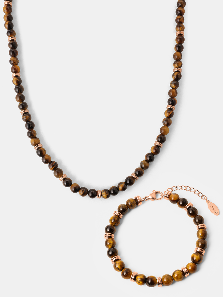 Halskette und Armband mit runden Tigerauge-Perlen, roséfarbenen Metallringen und Verschluss vor hellem Hintergrund.