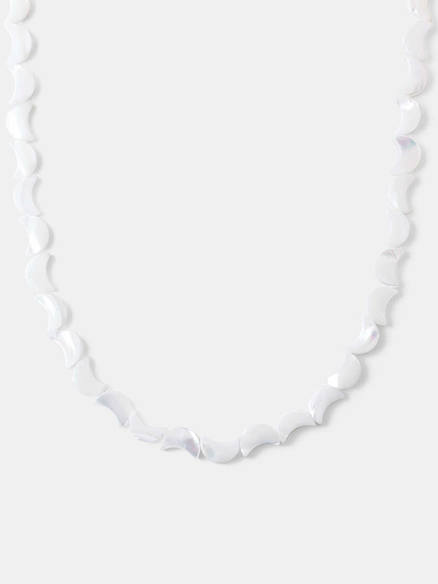 Silberfarbene Lunar Strand Kette mit bogenförmigen, opalisierenden Elementen vor hellgrauem, schlichtem Hintergrund als Nahaufnahme.