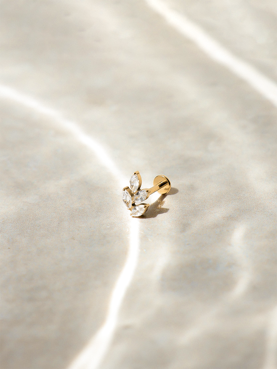 Goldener Stecker mit Blattmotiv und klaren Steinen, flacher Rückseite, vor Wasserhintergrund.
