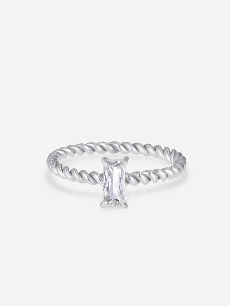 Silberfarbener Ring mit verdrehtem Seilband und rechteckigem, facettiertem Klarstein in Krappenfassung auf neutralem Untergrund.